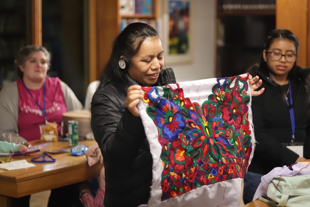 Woman holding up a brightly-colored embroidered blanket