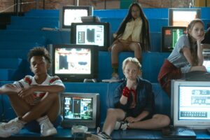 Four kids sitting on bleachers with computer monitors around them